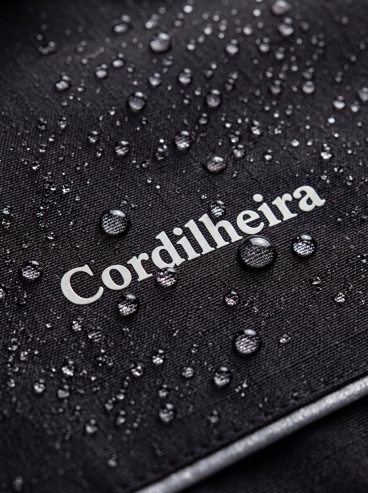 Close-up com gotas de água sobre o tecido e logo da Jaqueta Puffer 3 em 1 Cordilheira Hybrid Feminina, Roupa da Marca Cordilheira com Boa resistência, impermeabilidade e proteção Confiável para neve e atividades outdoor.