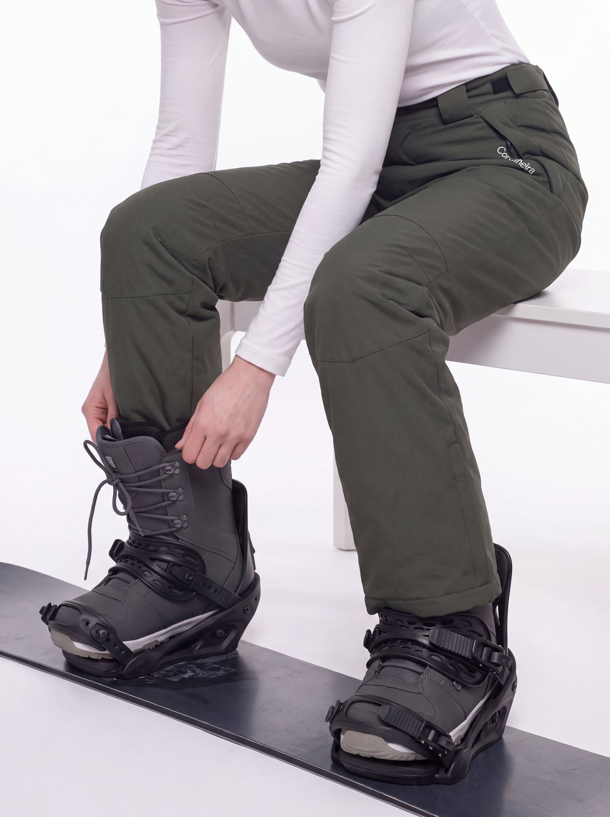 Pessoa ajustando botas de snowboard com Calça 2 em 1 Cordilheira Pathfinder Feminina, Roupa da Marca Cordilheira com Boa resistência e uso Confiável para neve e frio.