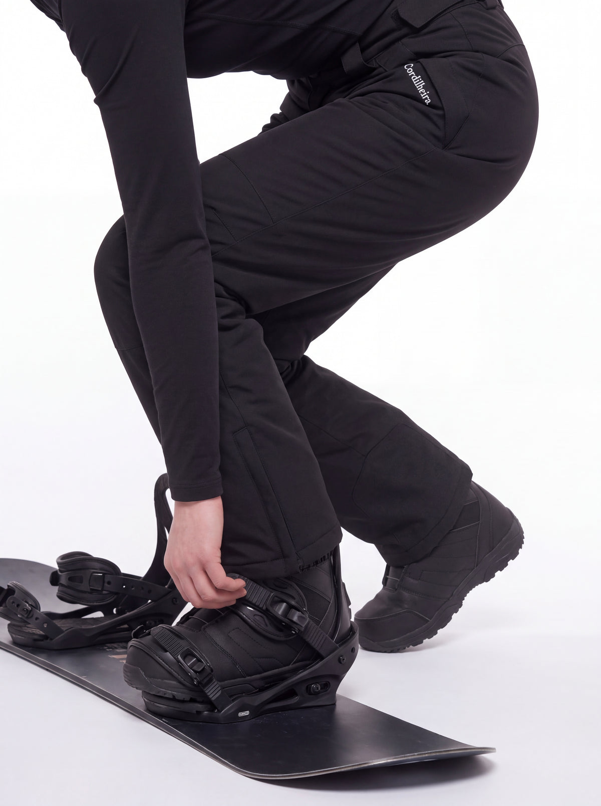 Pessoa colocando botas de snowboard com Calça 2 em 1 Cordilheira Pathfinder Feminina, Roupa da Marca Cordilheira com Boa proteção, resistência e uso Confiável para esportes na neve.