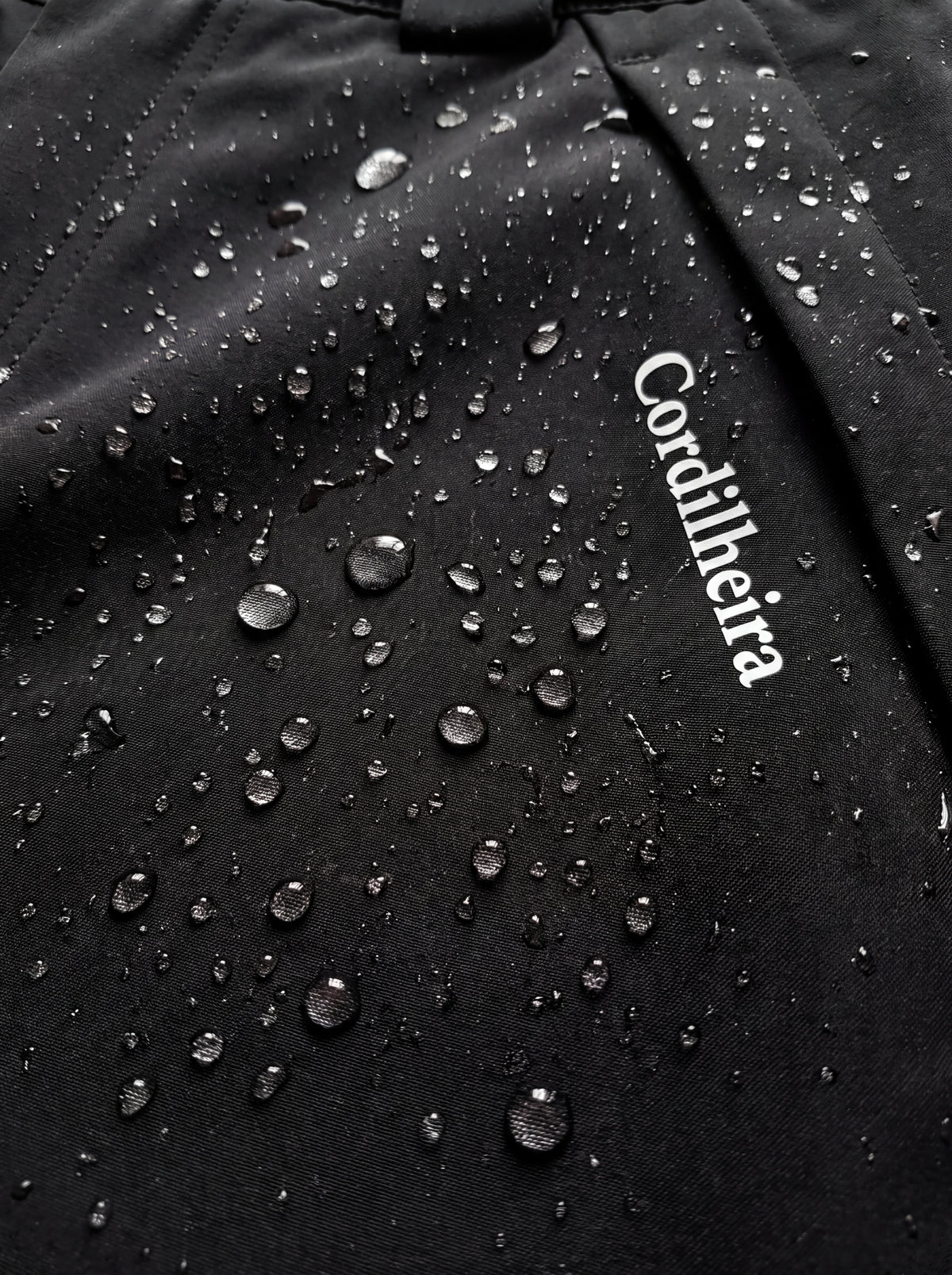 Close-up com gotas de água no tecido da Calça 2 em 1 Cordilheira Pathfinder Masculina, Roupa da Marca Cordilheira com Boa impermeabilidade, resistência e proteção Confiável para neve e umidade.